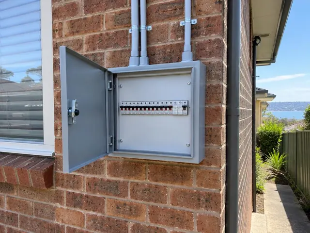 Open external switchboard on a brick house wall beside a window in Newcastle